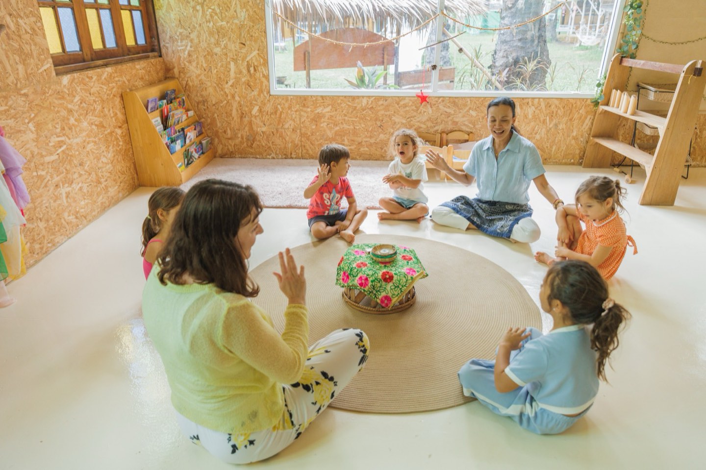 Two teachers and a group of young children sitting in a circle on the floor at Bamboo Valley, clapping and singing together during morning circle