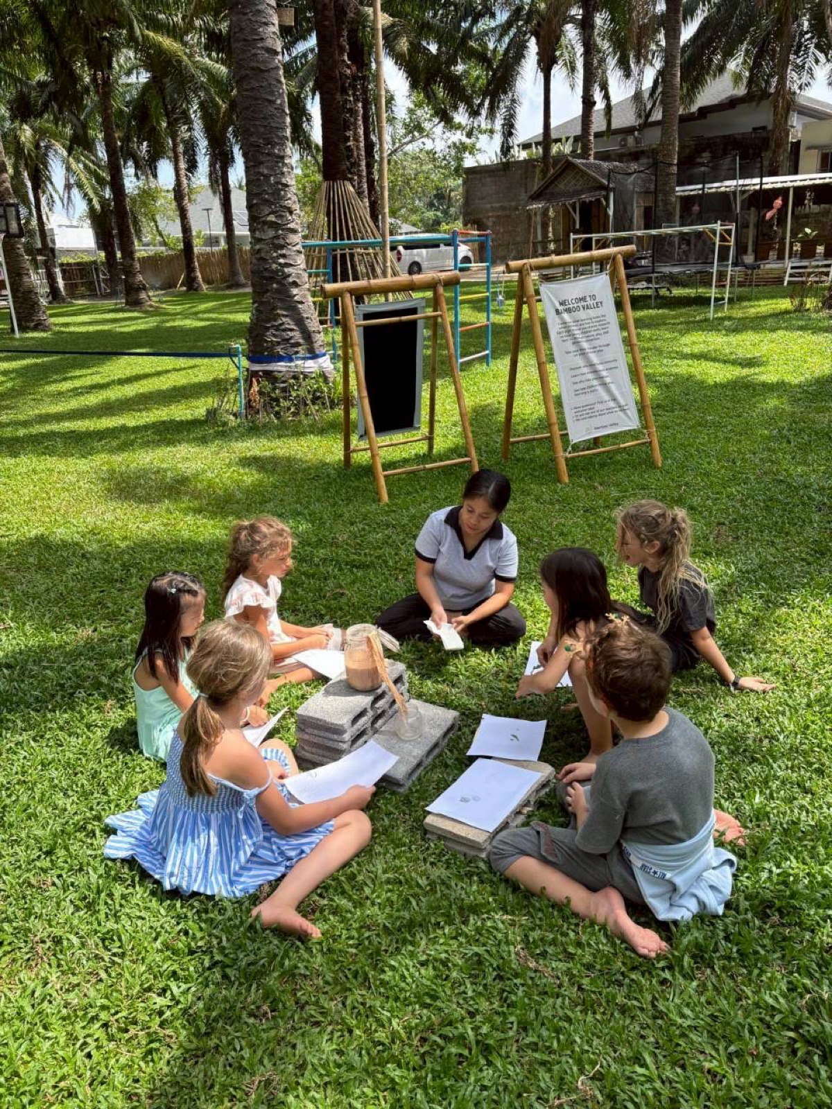 Children gathered in an outdoor reading circle under the palm trees at Bamboo Valley