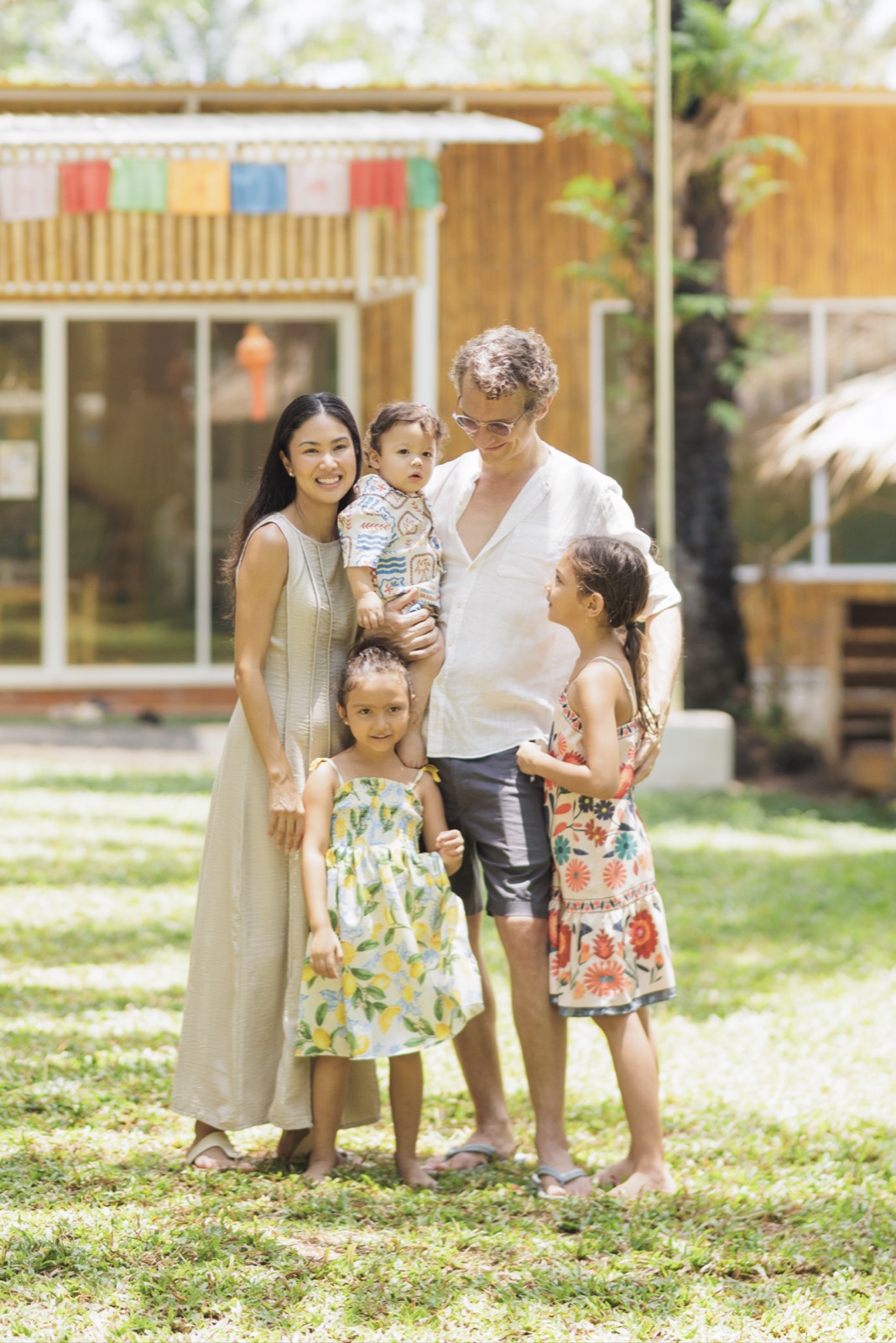 Bamboo Valley founders Marc and Nutthanit Schwyn with their three children outside a school building with prayer flags overhead