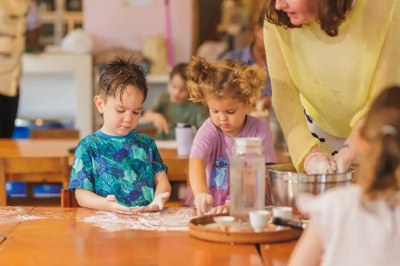 Two children kneading dough in flour with a teacher