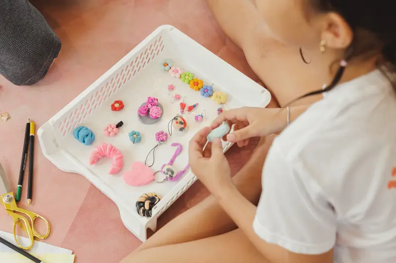A child shaping small clay flowers and charms on a tray