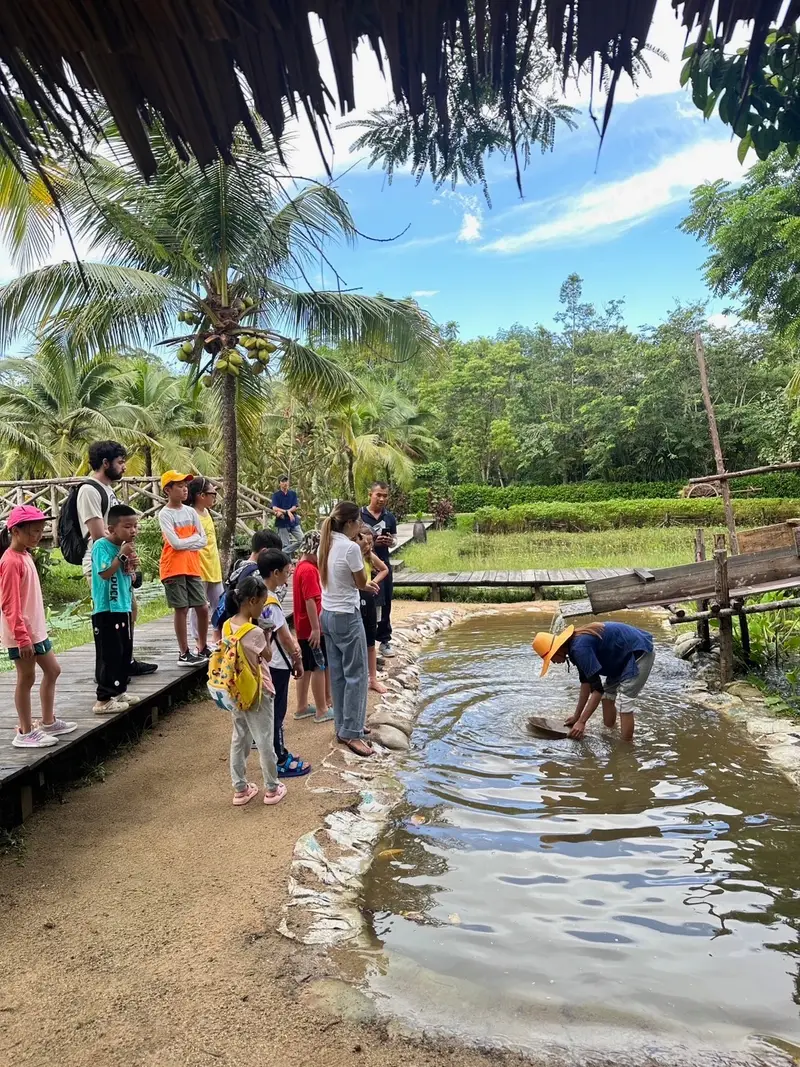 Children on a field trip watching a farmer pan for tin in a stream