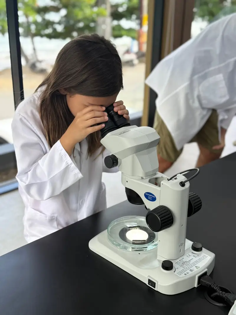 A girl in a lab coat looking through a microscope on a field trip by the sea