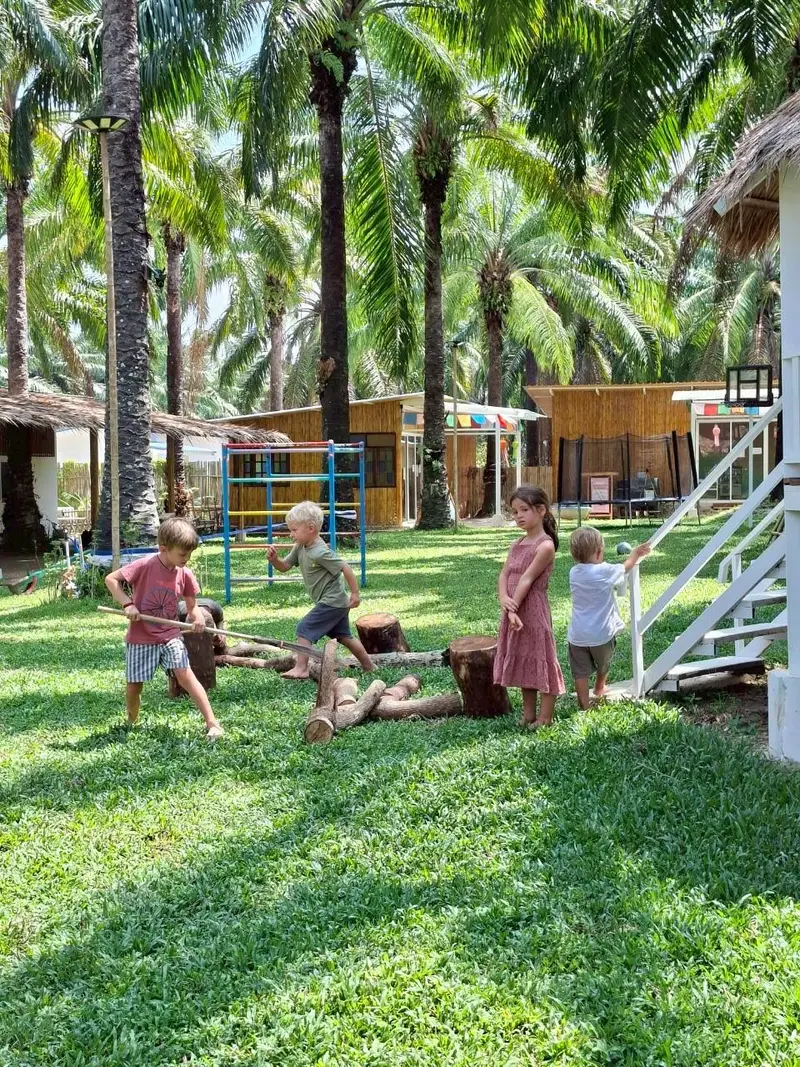 Children playing on logs on the lawn under the palm trees of our nature park