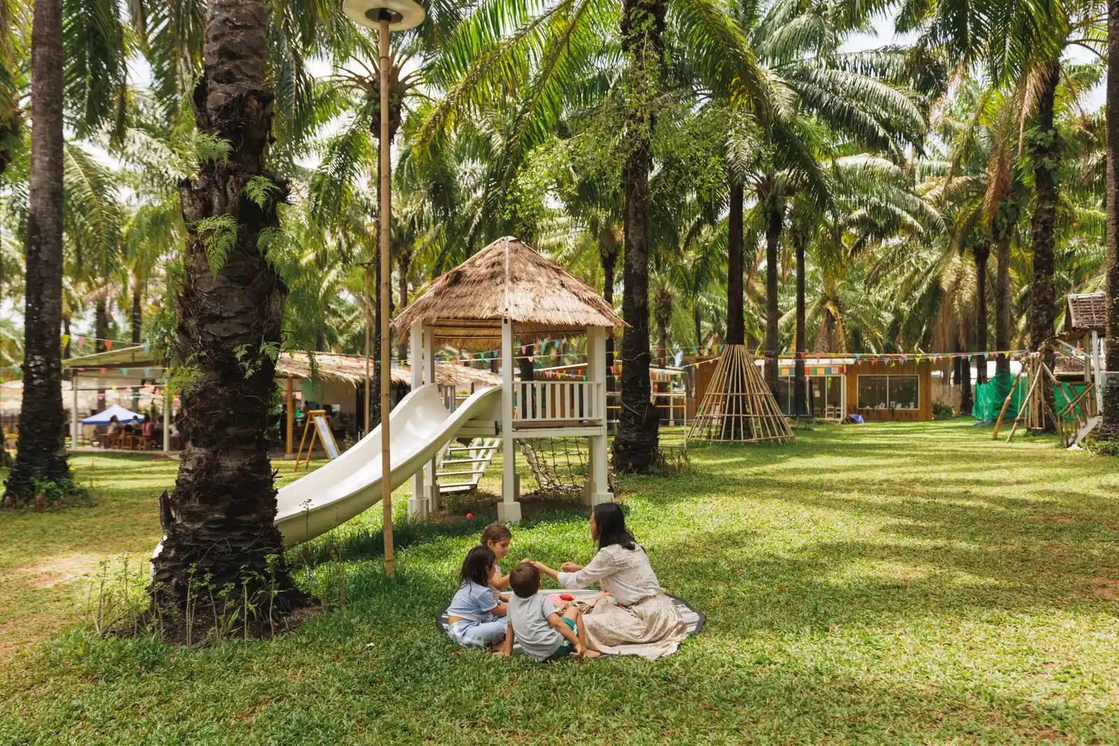 A teacher reading with children on a mat on the lawn under the palm trees at Bamboo Valley