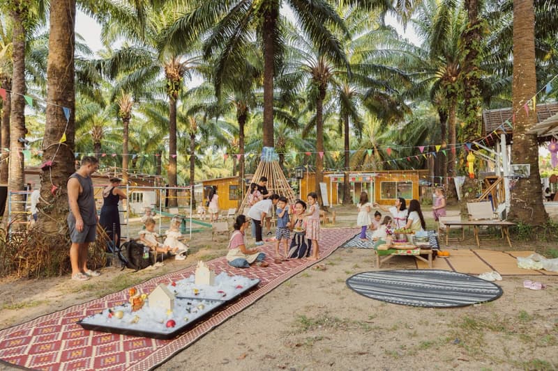 Families and children at the market under the palm trees, with bunting overhead