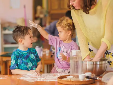 A girl sprinkling flour on a boy at the baking table, both laughing