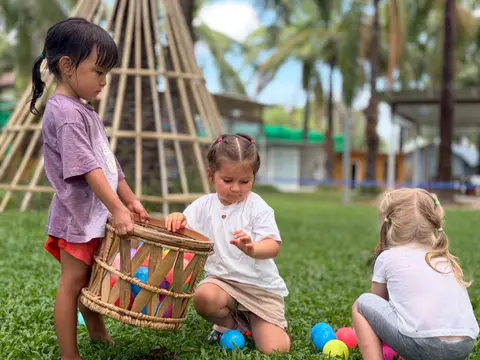 Three children playing with a basket and balls on the lawn