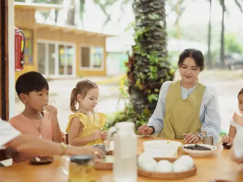 A teacher eating with children at a low wooden table