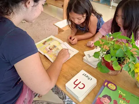 A teacher and two girls with a phonics card and a picture book