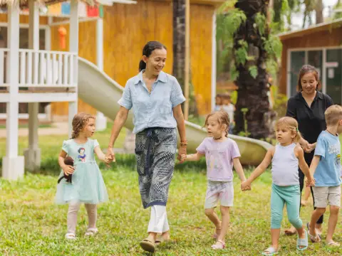 Teachers walking hand in hand with children across the lawn