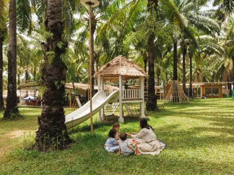 A teacher and children resting on a mat under the palms