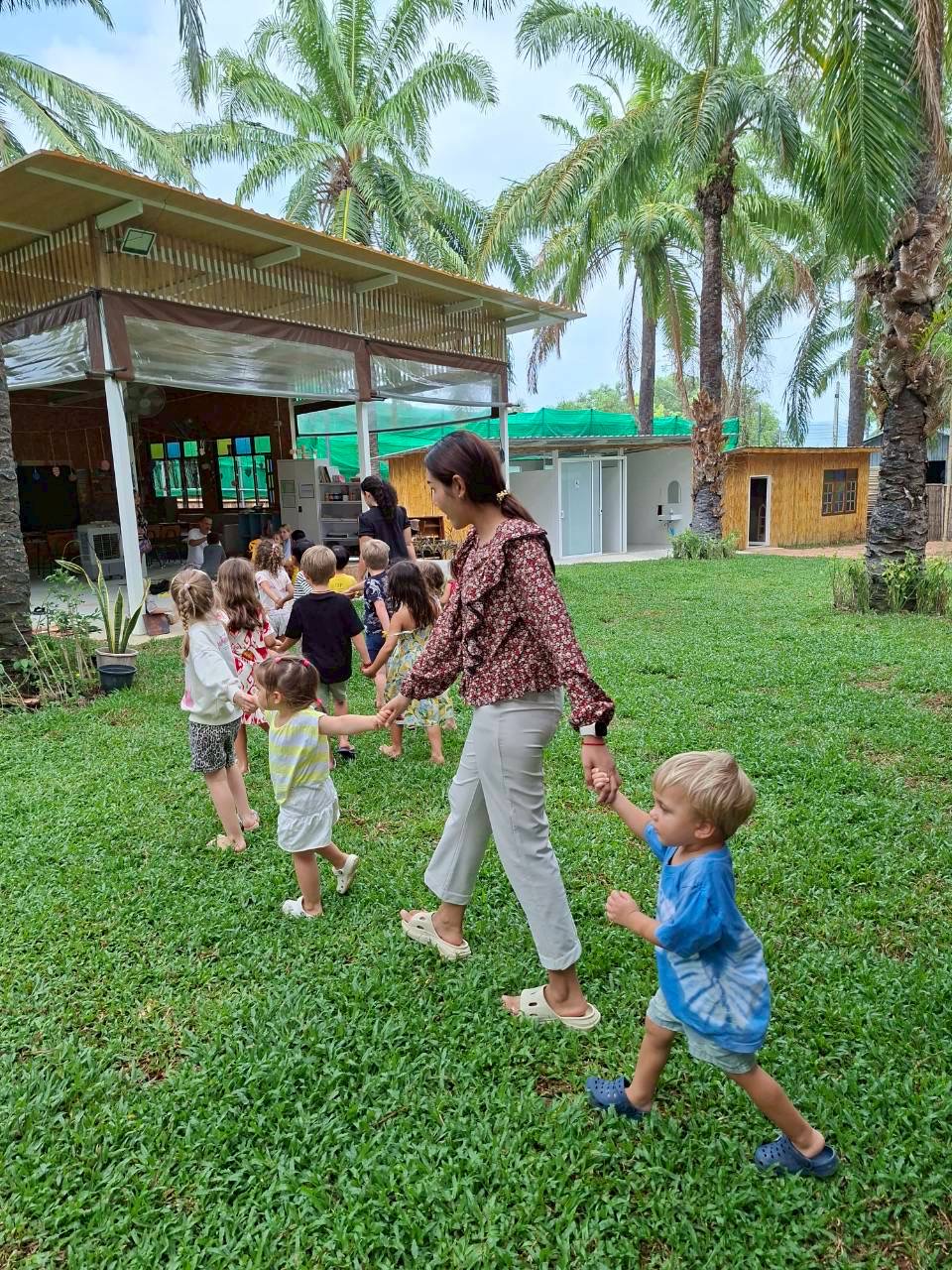 Children doing a ring dance together on green grass under palm trees
