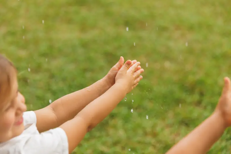 Small hands catching drops of water against green grass