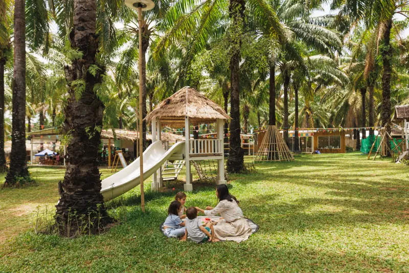 A teacher reading to children on a mat under the palms