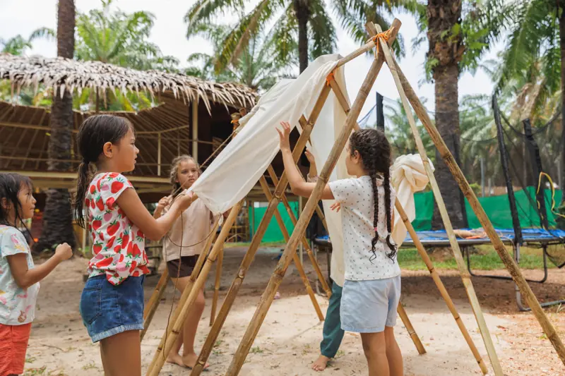 Three girls and a teacher draping fabric over a bamboo tipi they built