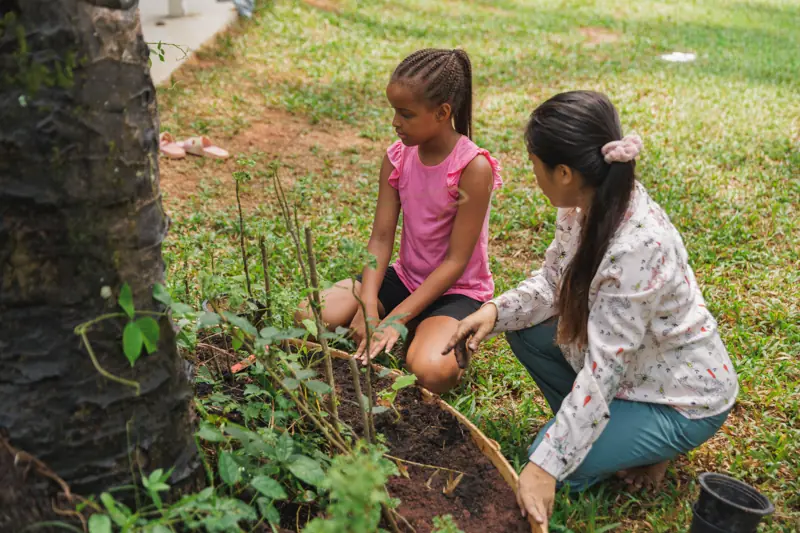 A girl and her teacher studying plants at the base of a palm