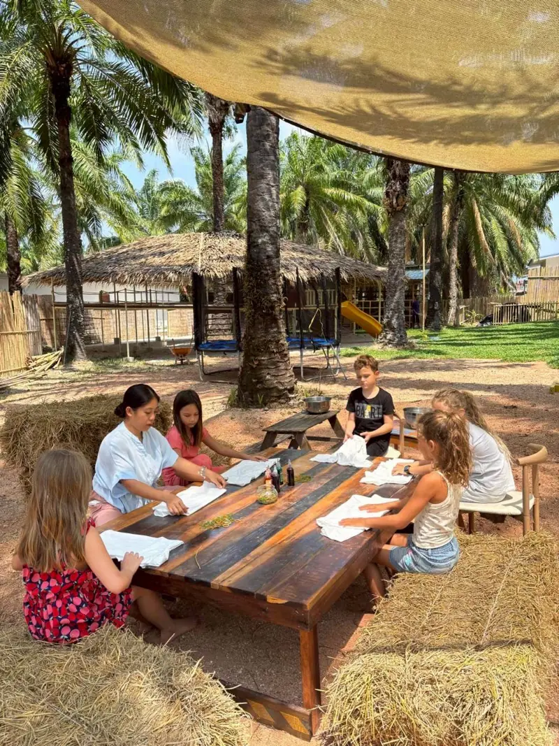 Older children working at a long wooden table under a shade sail