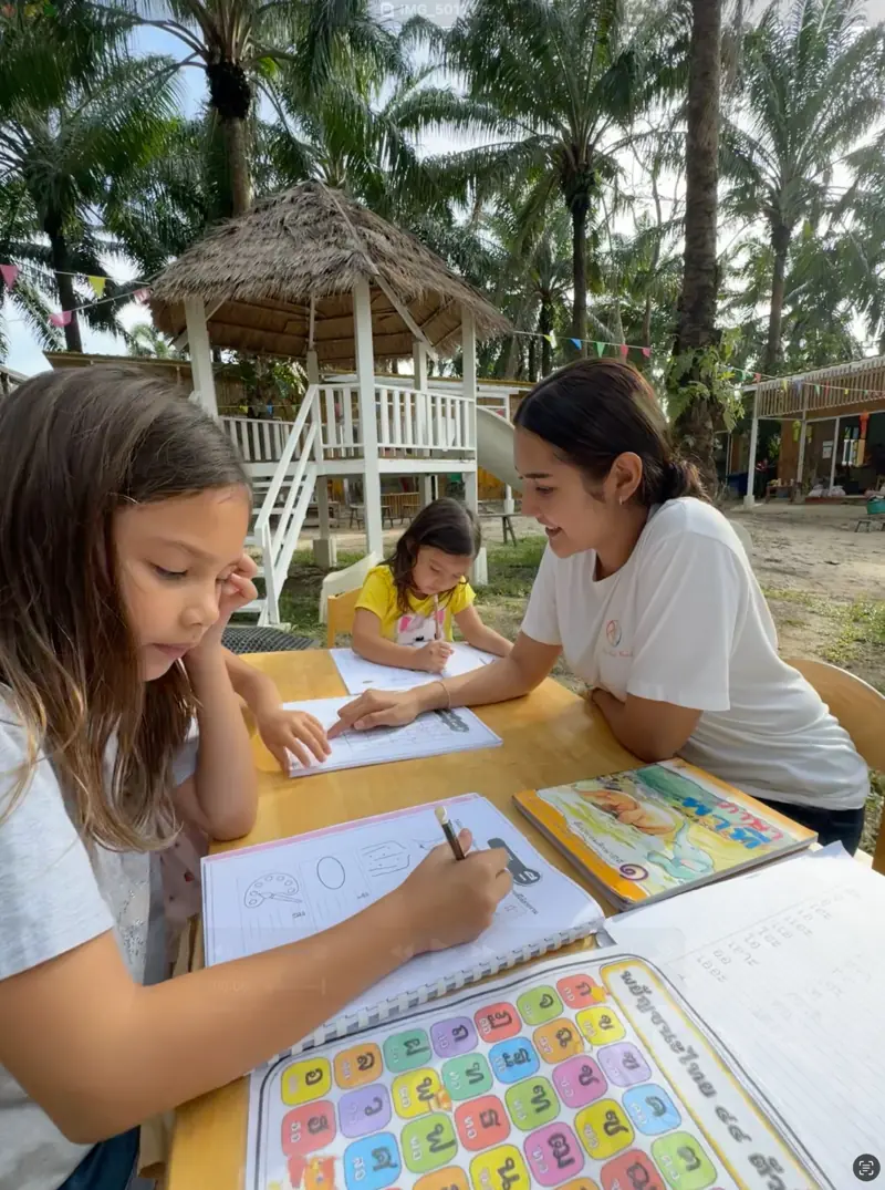 A girl writing in a workbook with her teacher at an outdoor table
