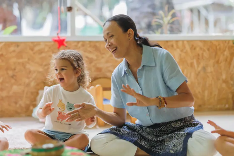 A teacher laughing with a delighted child at circle time