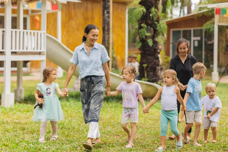 A teacher beaming as she walks with children
